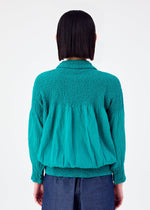 A person with straight, shoulder-length dark hair is seen from behind wearing the BALLOON CAULIFLOWER cardigan by me ISSEY MIYAKE in teal, paired with dark blue pants against a plain white background.