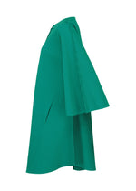 A side view of the SWING PLEATS dress by me ISSEY MIYAKE in bright green, featuring fine knit pleats and a cape-like sleeve flowing from shoulder to knee-length hem.