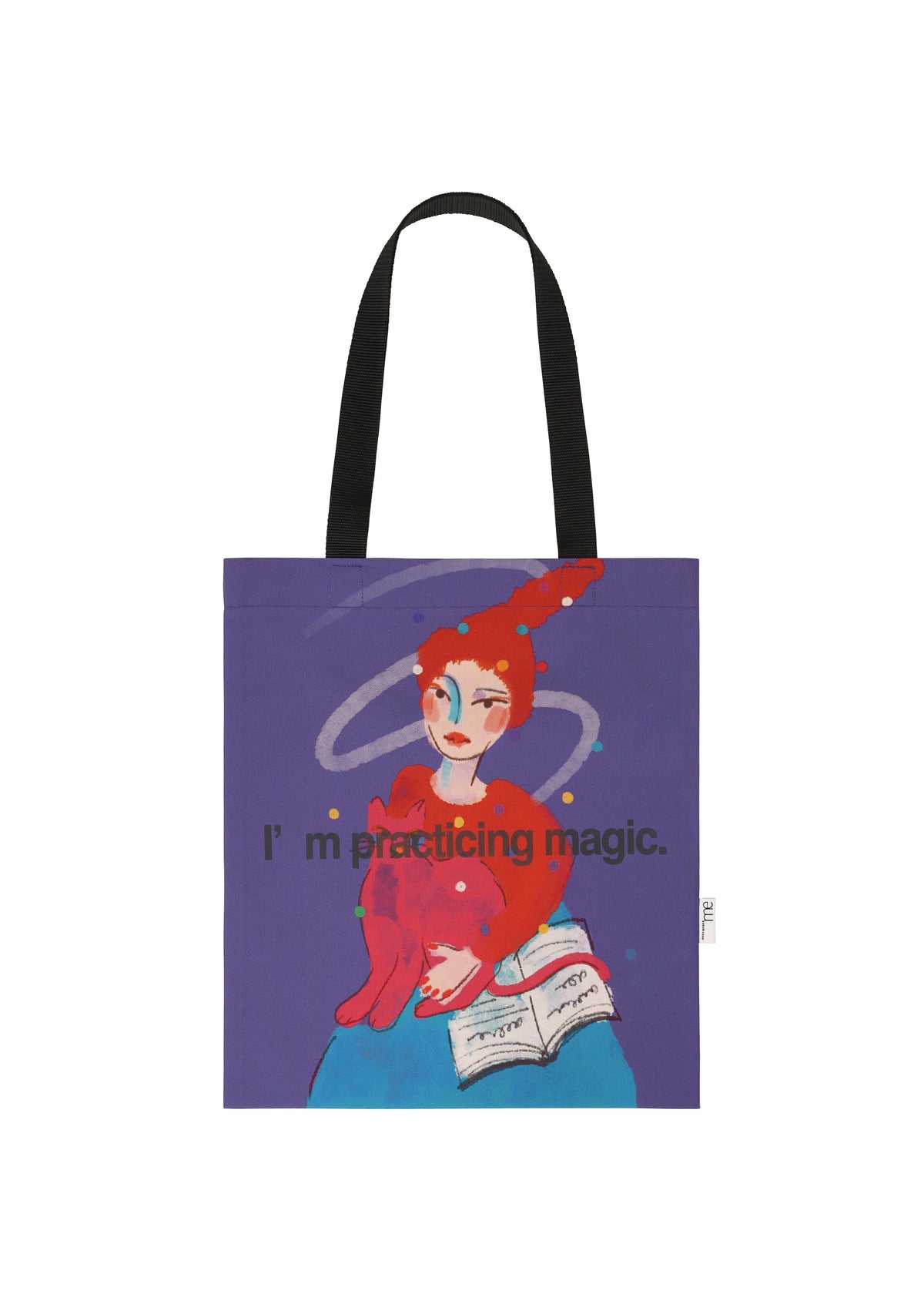 The CAT BAG by me ISSEY MIYAKE features black handles and a whimsical print: a person in a red hat holding a pink cat and spell book, with “I’m practicing magic” on a purple background—a playful choice for any aspiring mage. view 2 of 4