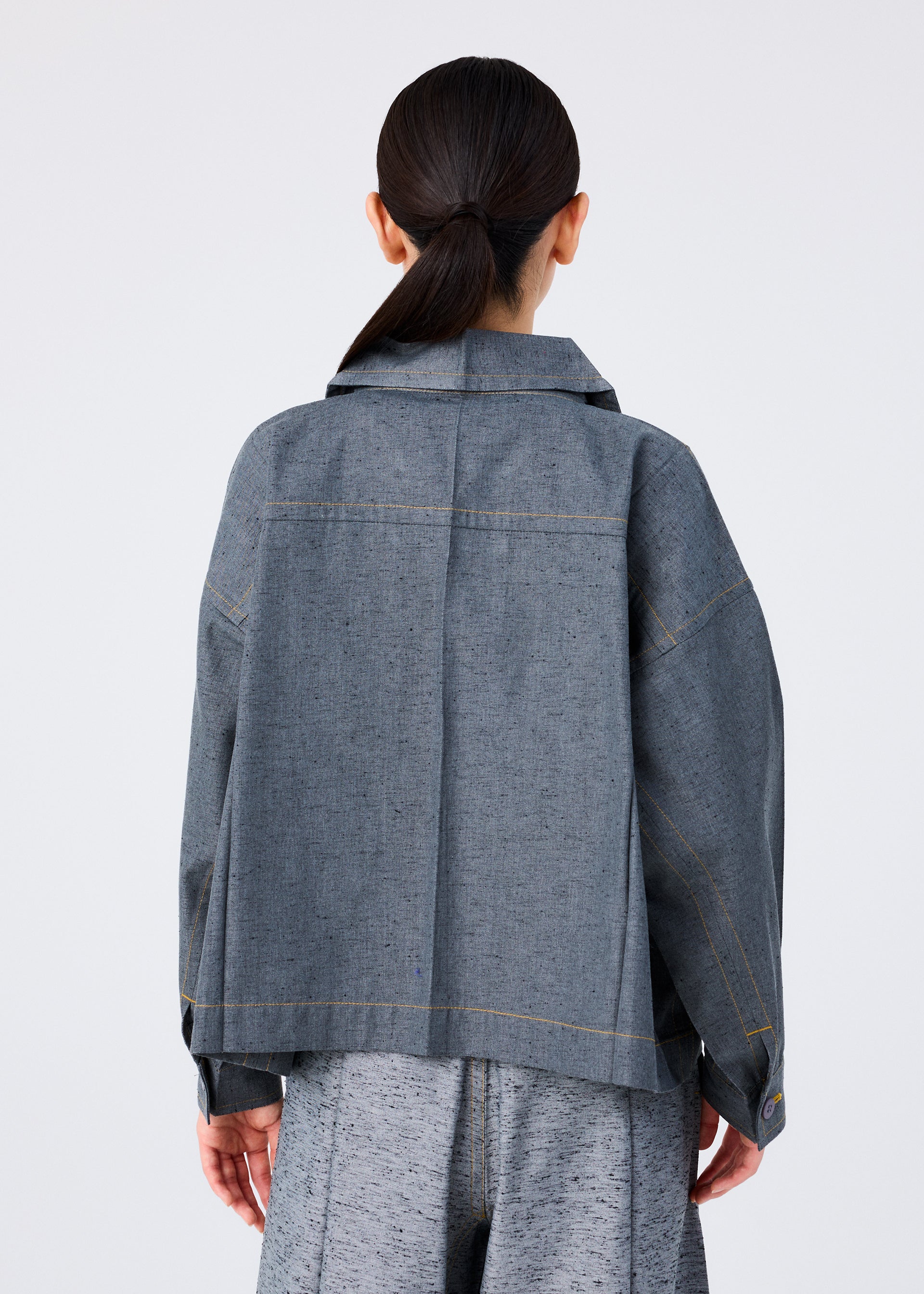 Zoomed view A person with long dark hair in a low ponytail is shown from the back, wearing a loose-fitting me ISSEY MIYAKE REmeTEX NEP DENIM jacket and matching gray pants against a plain light background.