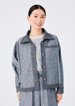 A woman with straight black hair smiles, wearing the me ISSEY MIYAKE REmeTEX NEP DENIM reversible grey jacket over a patterned white top and matching grey skirt, posing against a plain white background.