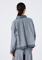 A person with dark hair in a low ponytail is shown from behind, wearing a loose-fitting, reversible REmeTEX NEP DENIM jacket and matching pants by me ISSEY MIYAKE, made from gray textured fabric against a plain light background.