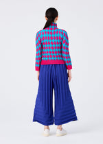 A person with long dark hair, seen from behind, wears a blue and pink argyle sweater and the COLOR PLEATS BOTTOM by me ISSEY MIYAKE—pleated, wide-leg royal blue pants—paired with white shoes against a plain white background.