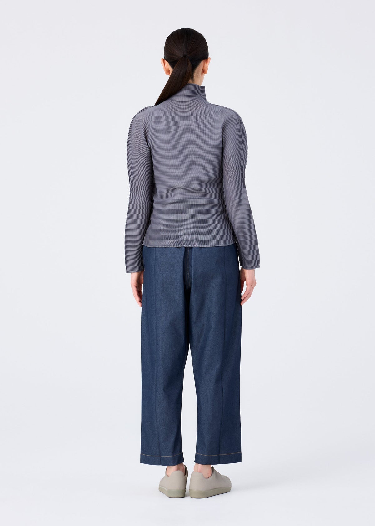 A person with long dark hair in a low ponytail, wearing a fitted gray turtleneck and me ISSEY MIYAKE FLAT DENIM wide-leg jeans, stands facing away in beige shoes against a plain white background. view 6 of 6