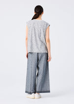 A woman stands with her back to the camera in me ISSEY MIYAKE's REmeTEX NEP DENIM wide-leg blue-gray pants, paired with a loose gray speckled sleeveless top and white shoes against a plain white background.