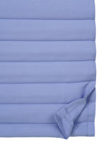 Close-up of RIPPLE PLEATS by me ISSEY MIYAKE in light blue, featuring quilted fabric with horizontal stitching and subtle handmade pleats. The bottom right corner is folded upward to reveal the underside.