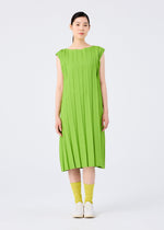 A woman faces forward in the CROSS PLEATS knee-length dress by me ISSEY MIYAKE, featuring bright green hand-pleating and cap sleeves. She pairs it with yellow socks and white shoes against a plain, light background.