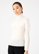 A woman with long dark hair tied back models the STRETCH PLEATS by me ISSEY MIYAKE—a white high-neck top and black pants—standing against a plain white background, looking at the camera with a slight smile.