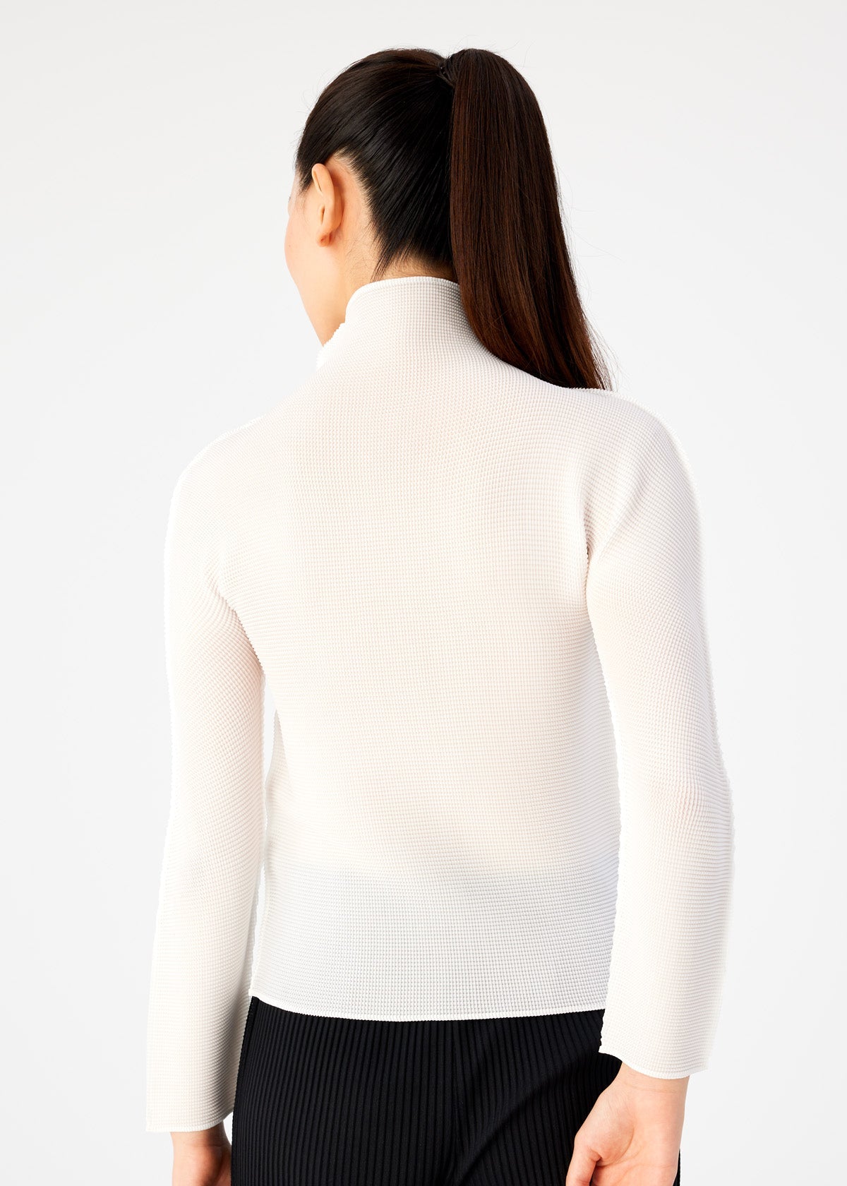 Zoomed view A woman with a ponytail is seen from behind, wearing the STRETCH PLEATS long-sleeved, high-neck top by me ISSEY MIYAKE and dark pinstriped pants, set against a plain light background.