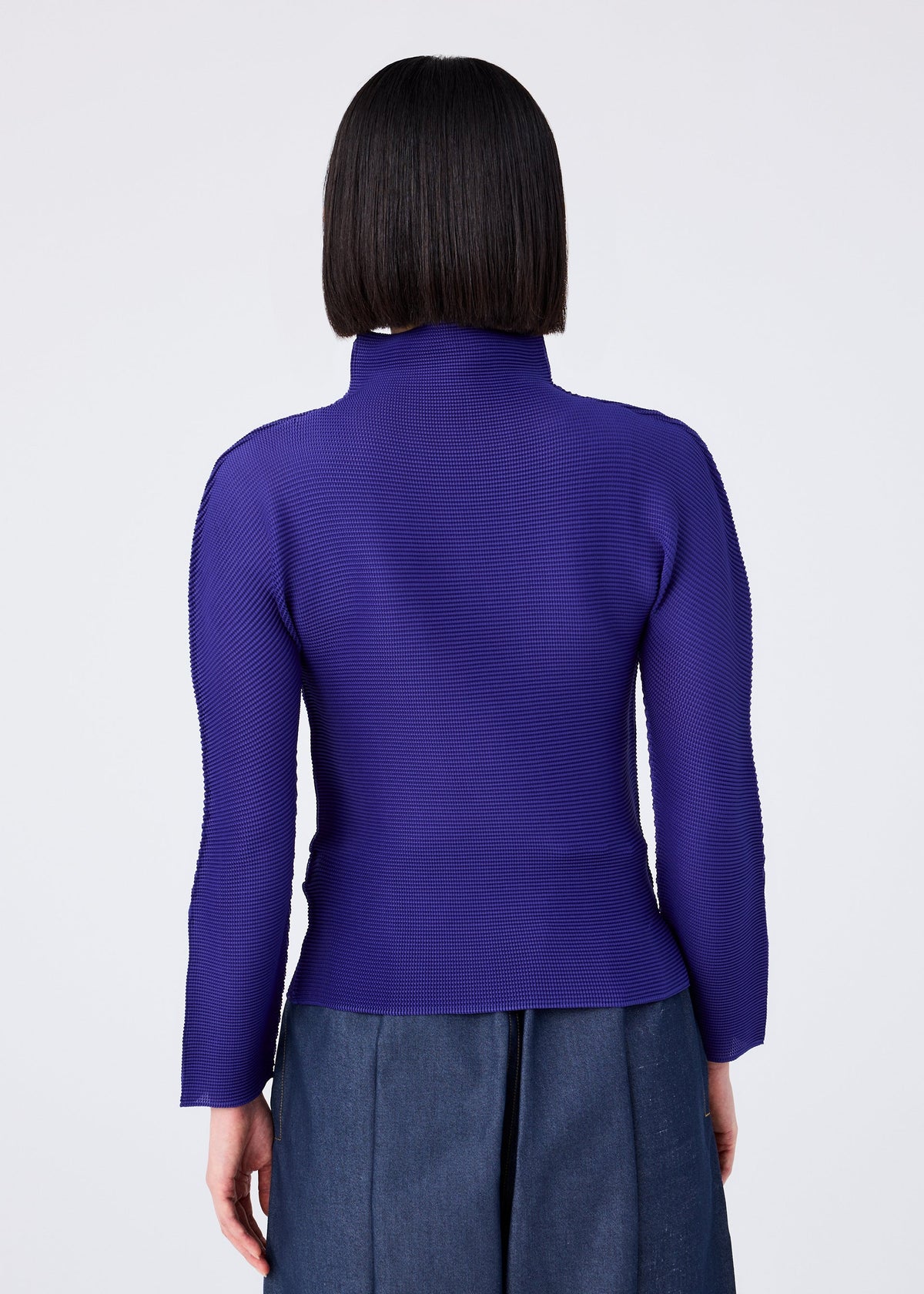 A person with straight, chin-length dark hair is shown from the back, wearing the me ISSEY MIYAKE STRETCH PLEATS 1 long-sleeved purple top and high-waisted blue pants against a plain light background. view 6 of 7