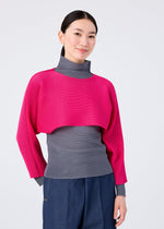 A woman wears the me ISSEY MIYAKE DOLMAN STRETCH PLEATS 1 sweater in pink and grey, featuring relaxed dolman sleeves and stretch pleats.