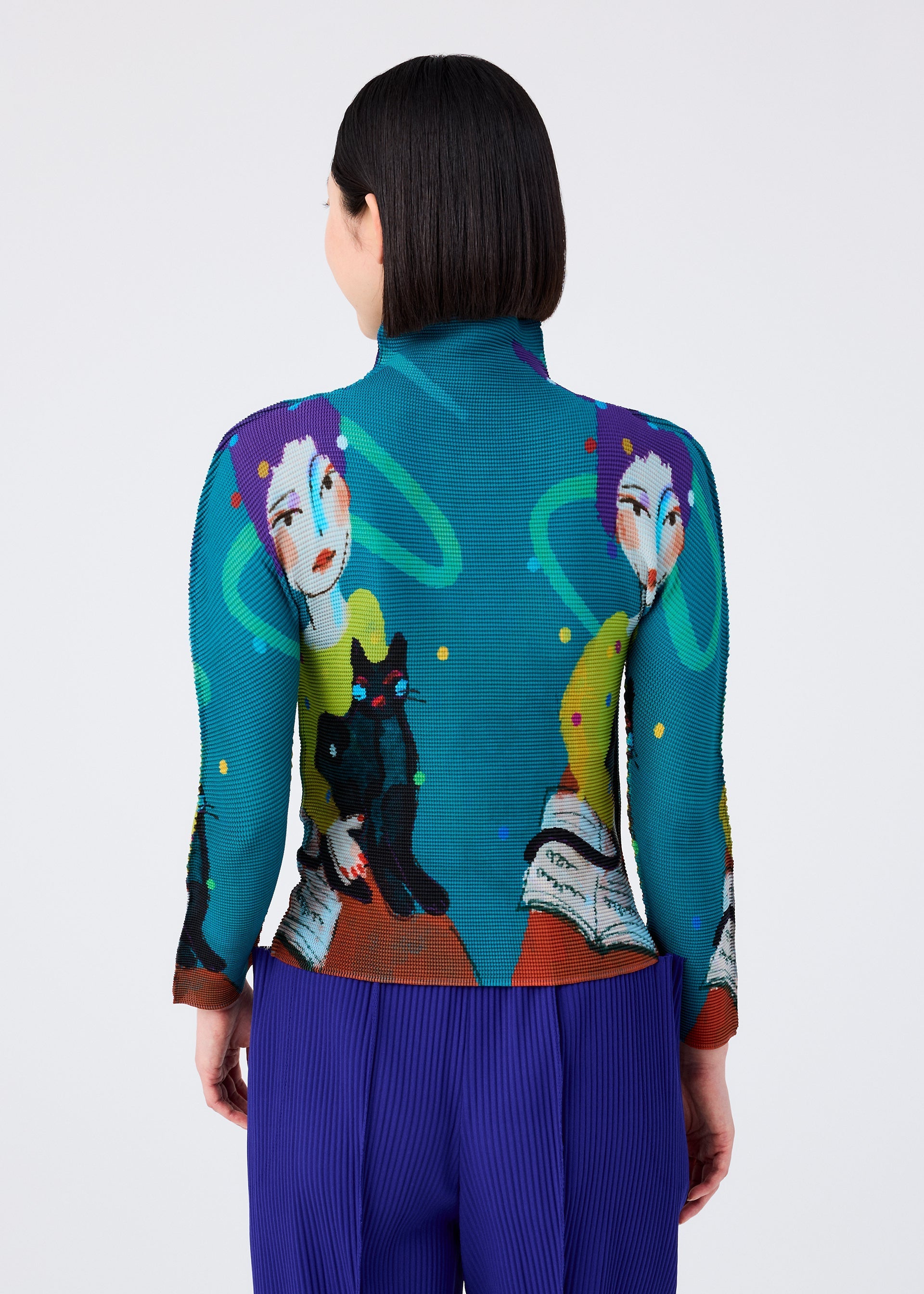 Zoomed view A person with short dark hair, seen from behind, wears the "CAT" high-neck long-sleeved top by me ISSEY MIYAKE featuring artistic faces, a black cat, and books, paired with blue pleated pants.