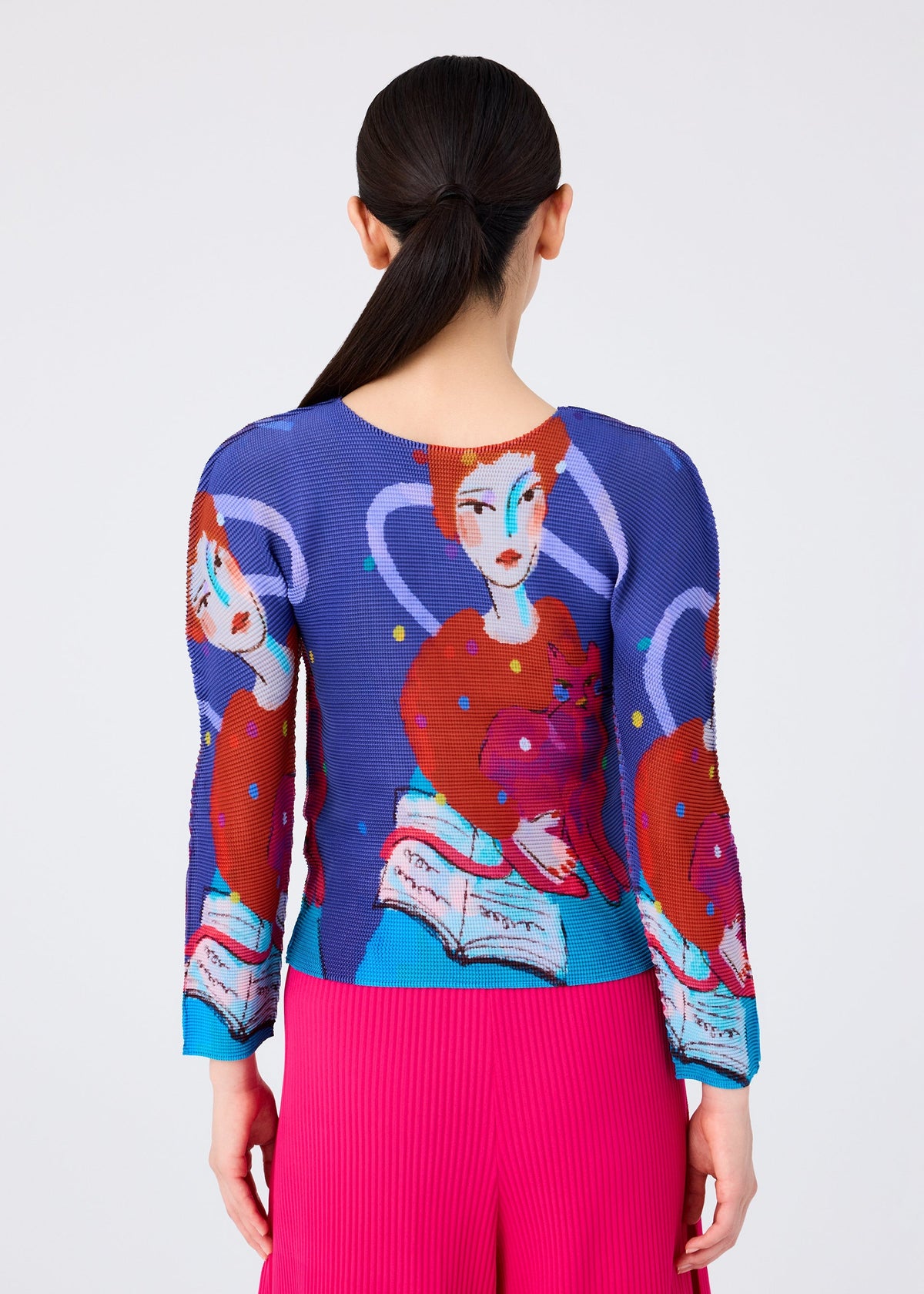 A person with long dark hair in a low ponytail is seen from behind, wearing the me ISSEY MIYAKE "CAT" blue stretch pleats top with an artistic woman-and-cat illustration, paired with bright pink pleated pants. view 6 of 7