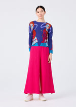 A woman faces forward in the me ISSEY MIYAKE CAT pleated long sleeve top with an artistic design and bright pink wide-leg pants, hair tied back, and light shoes, standing against a plain white background.