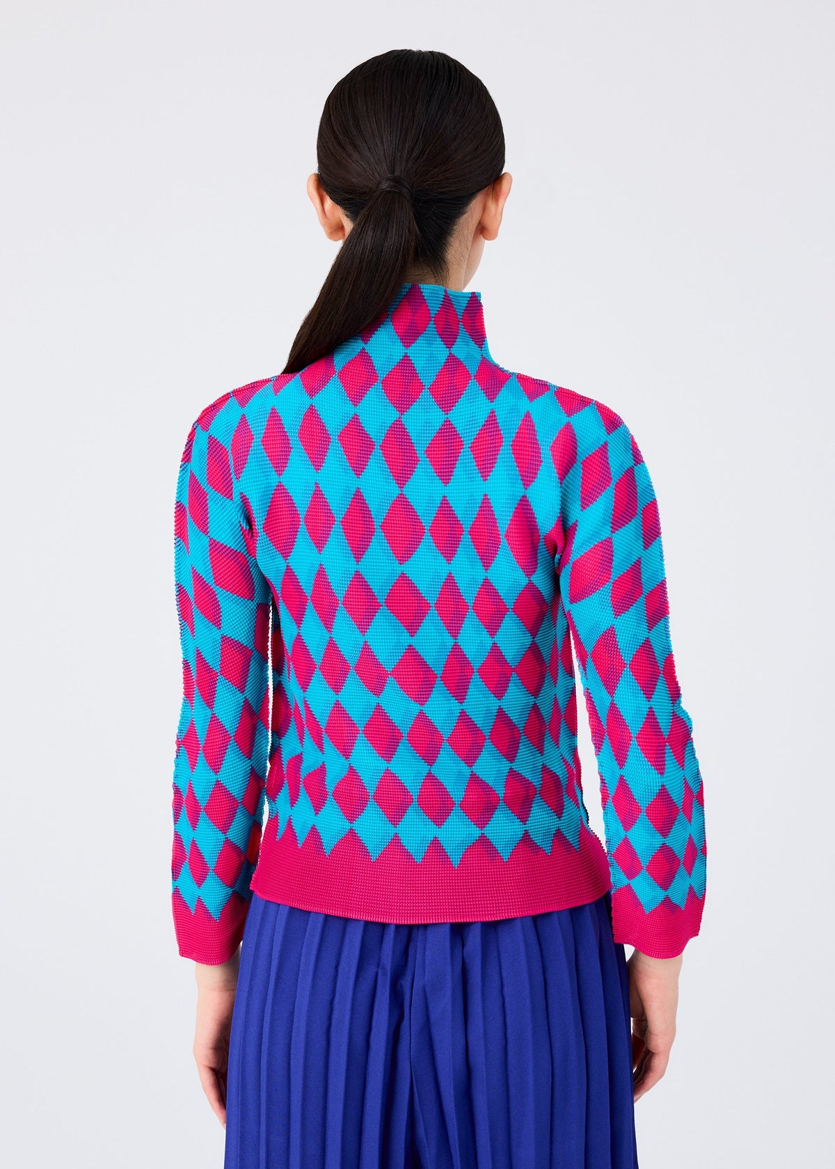 A person with long dark hair in a low ponytail is shown from the back, wearing the DIAMOND high-neck, long-sleeved top by me ISSEY MIYAKE with a pink and blue diamond motif and a pleated blue skirt against a plain light background. view 5 of 6