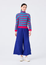 A woman stands against a white background wearing the DIAMOND high-neck long-sleeved top and wide-leg royal blue pleated pants by me ISSEY MIYAKE, paired with white slip-on shoes.