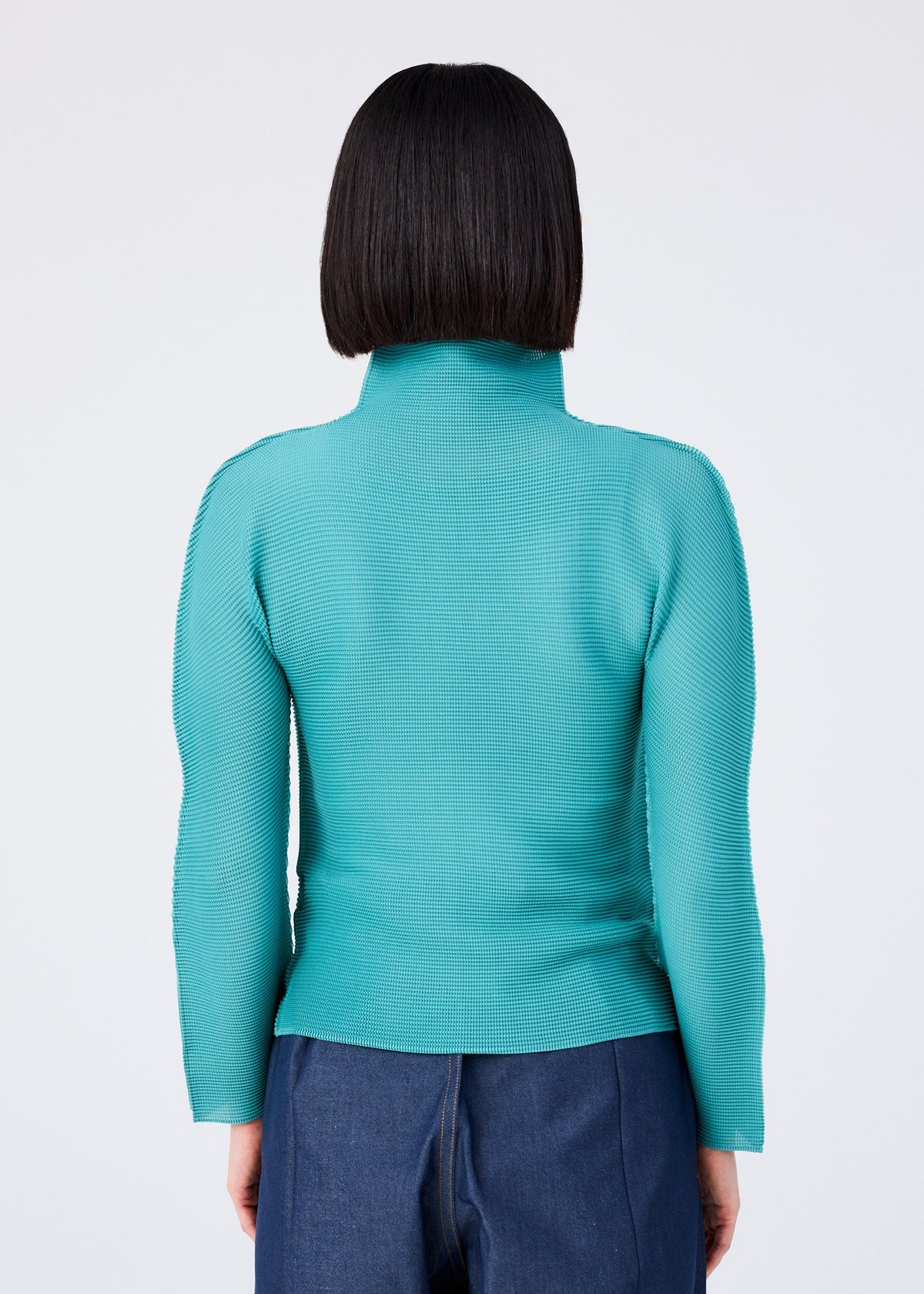 A person with straight, chin-length dark hair is seen from behind wearing the me ISSEY MIYAKE STRETCH PLEATS 2 teal long-sleeved top with stretch pleats and dark blue pants against a plain light background. view 6 of 7