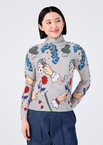 A woman with short black hair smiles in the MAGIC high-neck long-sleeved top by me ISSEY MIYAKE, featuring colorful cartoon illustrations and playful "MAGIC" lettering, paired with blue pants.