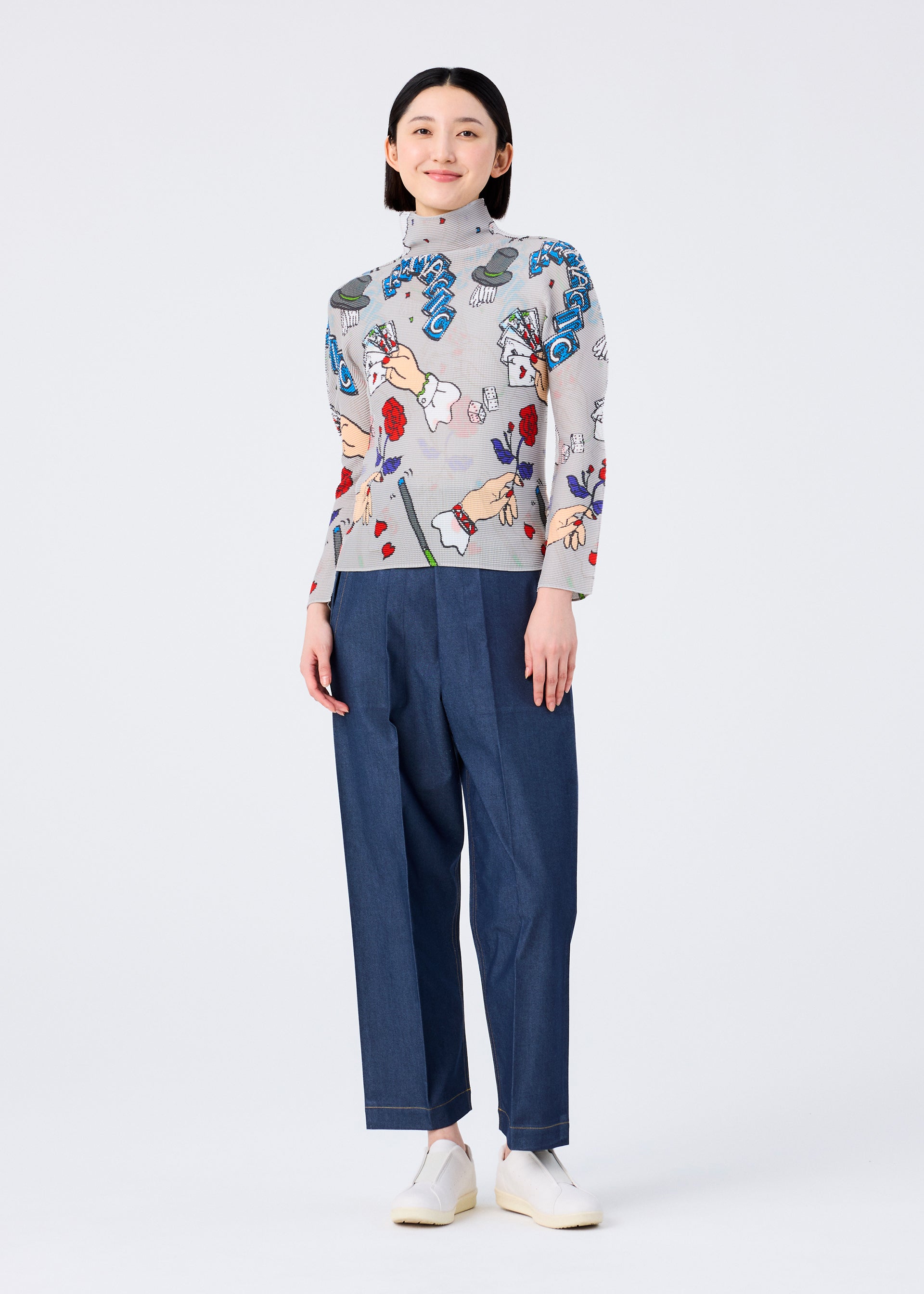 Zoomed view A person stands smiling in a MAGIC high-neck, long-sleeved top with colorful marker print by me ISSEY MIYAKE, blue high-waisted trousers, and white slip-on shoes against a plain white background.