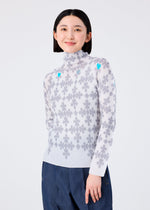 A woman with straight black hair smiles against a plain light background, wearing the me ISSEY MIYAKE SUIT: a high-neck, long-sleeved top with gray floral patterns and blue hearts, paired with blue pants.