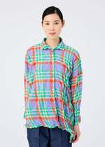 A person with dark hair tied back wears the me ISSEY MIYAKE CHECK WHIPPED PLEATS SHIRT, a colorful, loose-fitting summer top in green, orange, blue, and white tones paired with dark pants against a plain light background.