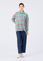 A person with dark hair tied back and a neutral expression wears the me ISSEY MIYAKE CHECK WHIPPED PLEATS SHIRT, featuring colorful yarn-dyed checks, paired with wide-leg blue pants and white shoes against a plain white background.