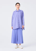 A person faces forward in the me ISSEY MIYAKE ANGLE PLEATS SHIRT, a lightweight, light purple long-sleeved top with diagonal stripes, paired with wide-leg blue trousers and white slip-on shoes against a plain white background.
