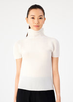 A woman with long dark hair pulled back wears me ISSEY MIYAKE STRETCH PLEATS black pants and a short-sleeved, high-neck top, standing against a plain white background and looking at the camera.