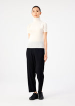 A woman stands against a white background wearing me ISSEY MIYAKE STRETCH PLEATS black pants, a short-sleeved high-neck top, and black slip-on shoes. She faces forward with a neutral expression and relaxed posture.