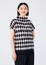 A woman with straight dark hair smiles and looks to the side, wearing the DIAMOND top by me ISSEY MIYAKE—a high-neck design with a black and white diamond motif—paired with black stretch pleated pants against a plain light background.