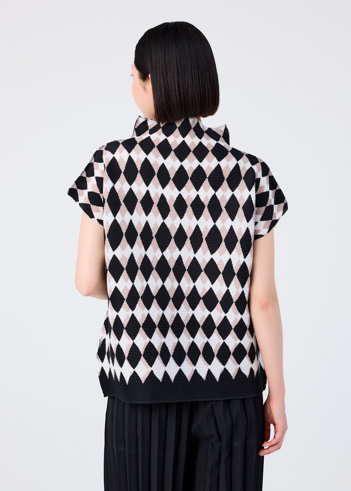 A person with short dark hair, seen from behind, wears the DIAMOND high-neck top by me ISSEY MIYAKE, featuring a black and light pink diamond pattern, paired with black pleated pants against a plain light background. view 5 of 6