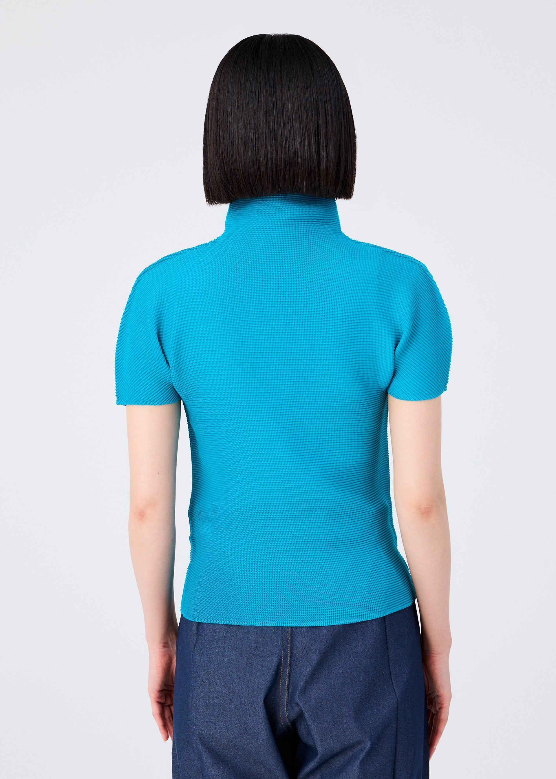 Zoomed view Seen from the back, a person with straight, chin-length dark hair wears the me ISSEY MIYAKE STRETCH PLEATS 3 bright blue short-sleeved, high-neck top and dark blue pants, standing against a plain white background.