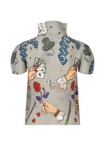 The MAGIC top by me ISSEY MIYAKE is a high-neck, short-sleeved style with puffed sleeves, featuring a playful magic marker print of hands, playing cards, dice, roses, magic hats, and “STARS” in blue on a light background.