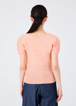 Seen from the back, a person with long dark hair in a low ponytail wears the me ISSEY MIYAKE STRETCH PLEATS 4 light peach short-sleeved top and dark blue pants against a plain light background.
