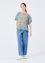 A person with long dark hair pulled back and a neutral expression wears the me ISSEY MIYAKE CHECK WHIPPED PLEATS SHIRT against a plain background, paired with light blue wide-leg pants and white slip-on shoes.
