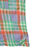 The CHECK WHIPPED PLEATS SHIRT by me ISSEY MIYAKE features lightweight, semi-sheer fabric with a multicolored yarn-dyed green, orange, blue, and white check pattern. The material is slightly wrinkled with a folded corner.