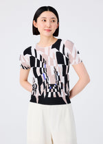 A woman with short dark hair wears the me ISSEY MIYAKE PERSPECTIVE geometric-patterned top and white STRETCH PLEATS pants, standing against a plain light background, looking slightly to the side and smiling gently.