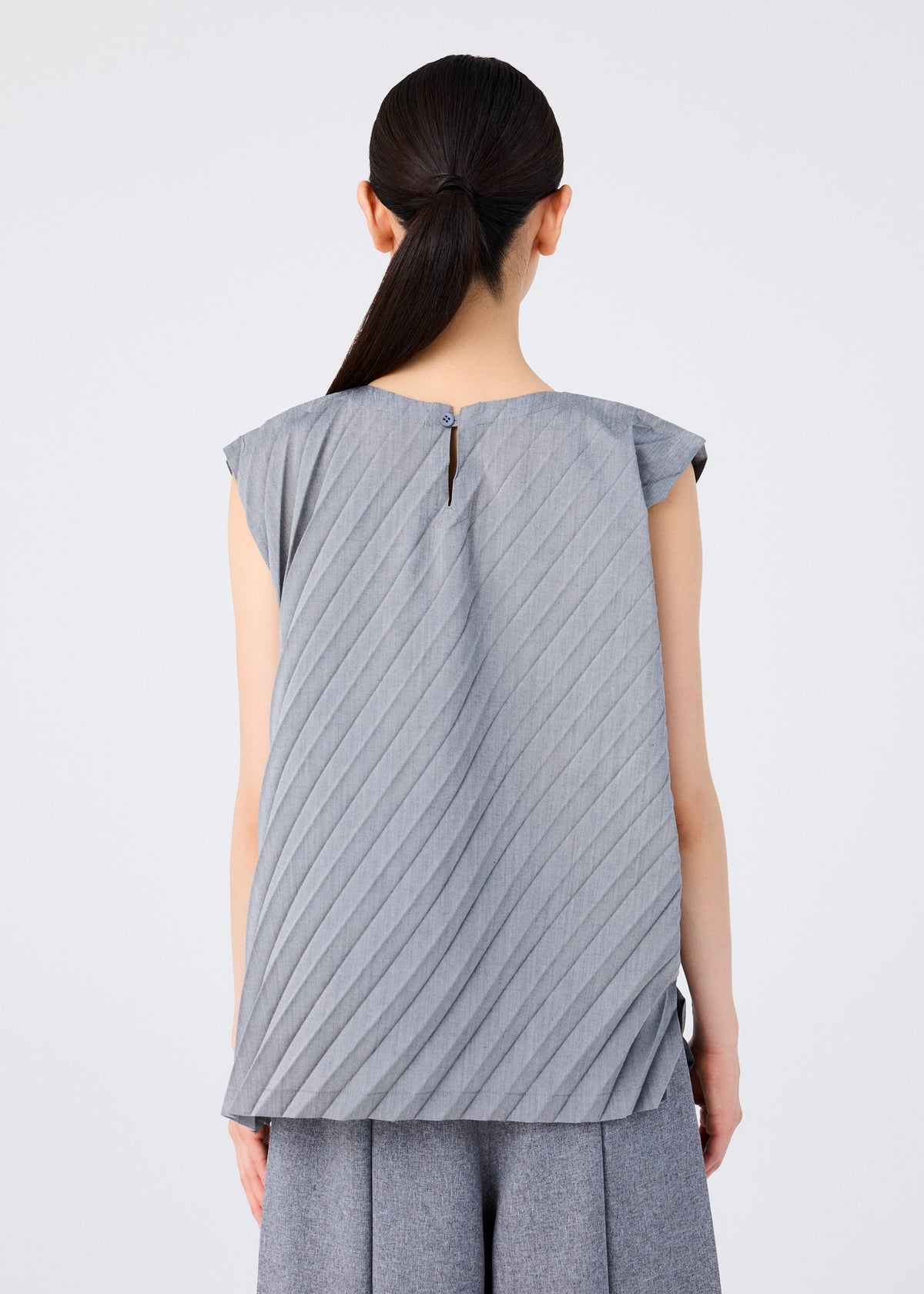 Back view of a woman wearing the me ISSEY MIYAKE ANGLE PLEATS SHIRT in gray, a sleeveless lightweight top with pleats and a single back button closure, styled with matching gray pants. view 7 of 9