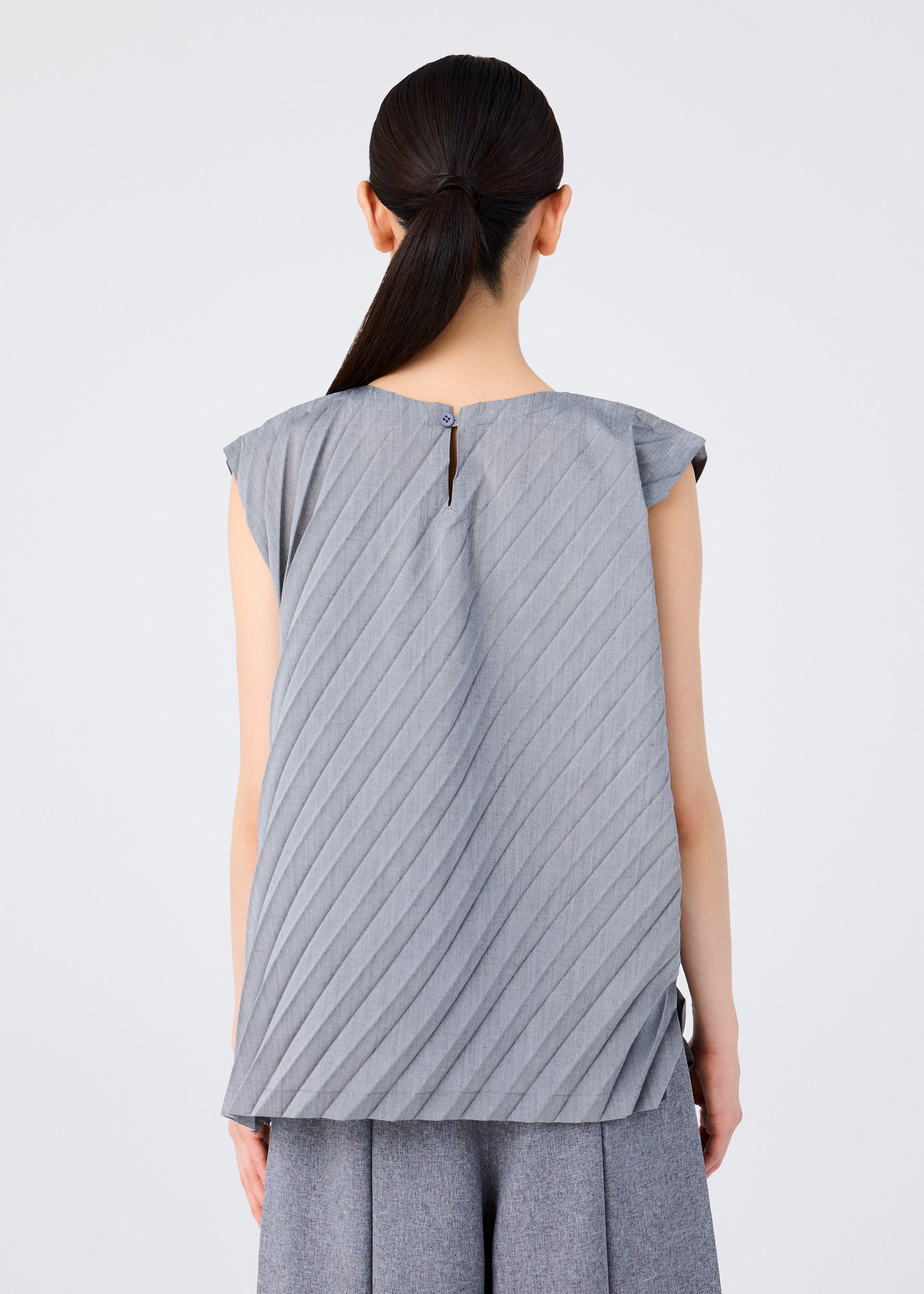 Zoomed view Back view of a woman wearing the me ISSEY MIYAKE ANGLE PLEATS SHIRT in gray, a sleeveless lightweight top with pleats and a single back button closure, styled with matching gray pants.