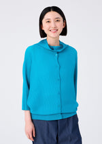 A woman with straight, chin-length black hair smiles at the camera, wearing the me ISSEY MIYAKE DOLMAN STRETCH PLEATS 2 bright blue long-sleeve cardigan and dark blue pants, standing against a plain white background.