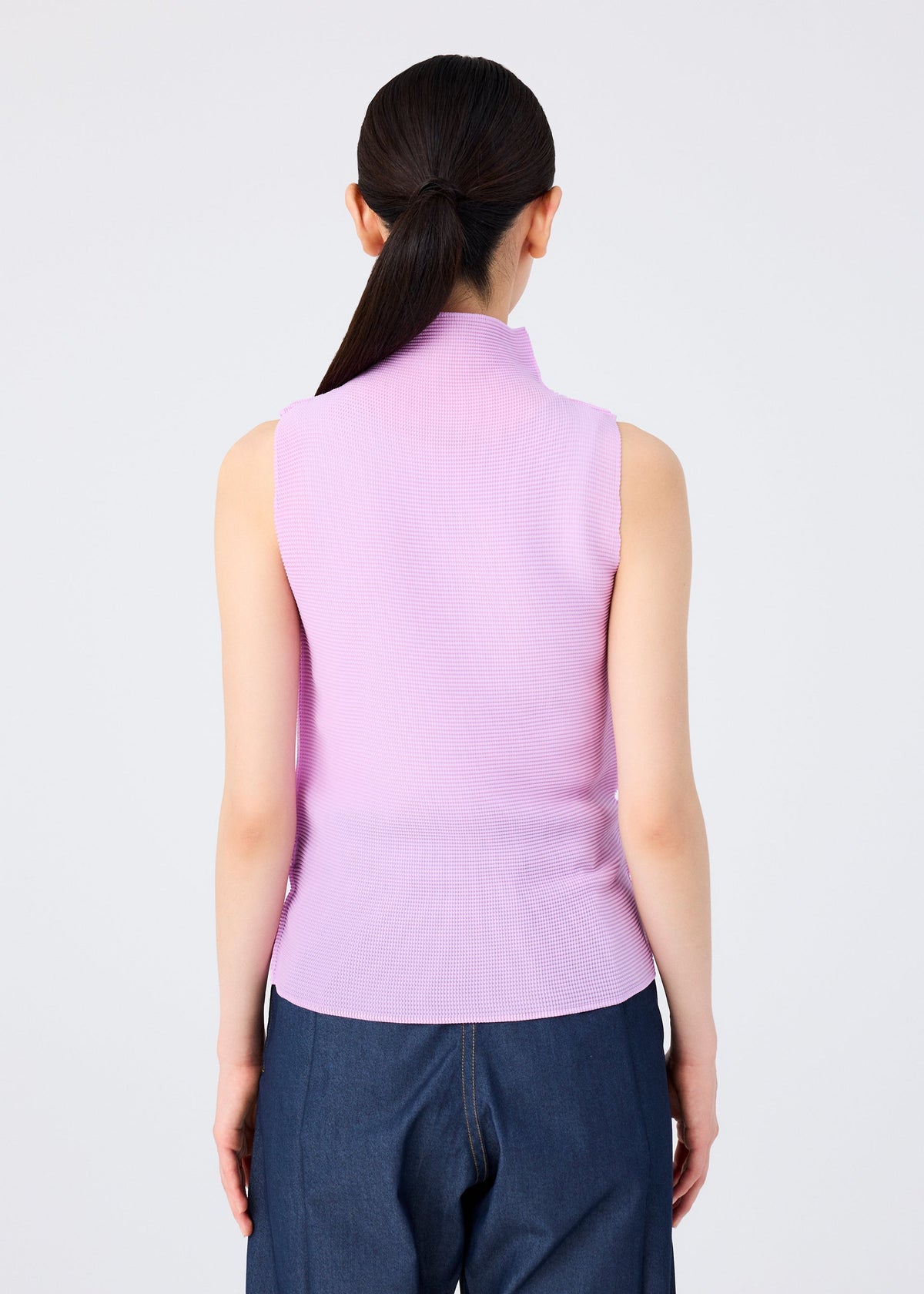 Seen from behind, a person with long dark hair in a low ponytail wears the me ISSEY MIYAKE STRETCH PLEATS 5 high-neck sleeveless top in light purple and dark blue pants, standing against a plain light background. view 6 of 7