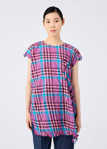 A woman with straight black hair, wearing the CHECK WHIPPED PLEATS SHIRT by me ISSEY MIYAKE in colorful pink, blue, and black checks with dark pants, stands facing forward against a plain light gray background with a neutral expression.