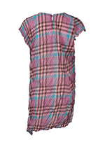The CHECK WHIPPED PLEATS SHIRT by me ISSEY MIYAKE is a short-sleeved, knee-length tunic dress with yarn-dyed checks, crinkled texture, and an asymmetrical hem in pink, blue, and black shades shown on a white background.