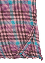 A close-up of the me ISSEY MIYAKE CHECK WHIPPED PLEATS SHIRT—a lightweight women’s tunic with a pink, purple, blue, and brown plaid pattern. The sheer summer fabric has slightly curled and wrinkled edges.