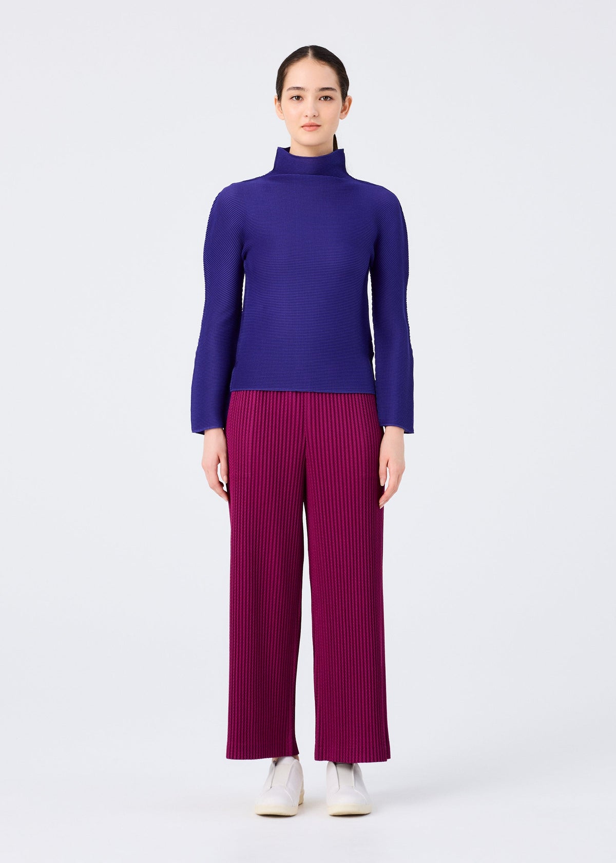 A person faces forward, wearing the WARM MESH PLEATS long-sleeve high-neck top and wide-leg pleated pants by me ISSEY MIYAKE, paired with white shoes. Their expression is neutral against a plain white background. view 5 of 6