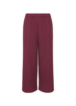 The WARM MESH PLEATS pants by me ISSEY MIYAKE feature a wide-leg, relaxed fit in deep burgundy with an elastic waistband and vertical ribbing. Subtle pleats add texture. Shown against a white background. - RASPBERRY （no.23）
