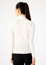A woman with long dark hair in a ponytail is seen from behind, wearing a white KNIT STRETCH PLEATS top from me ISSEY MIYAKE and black pants against a plain light background.
