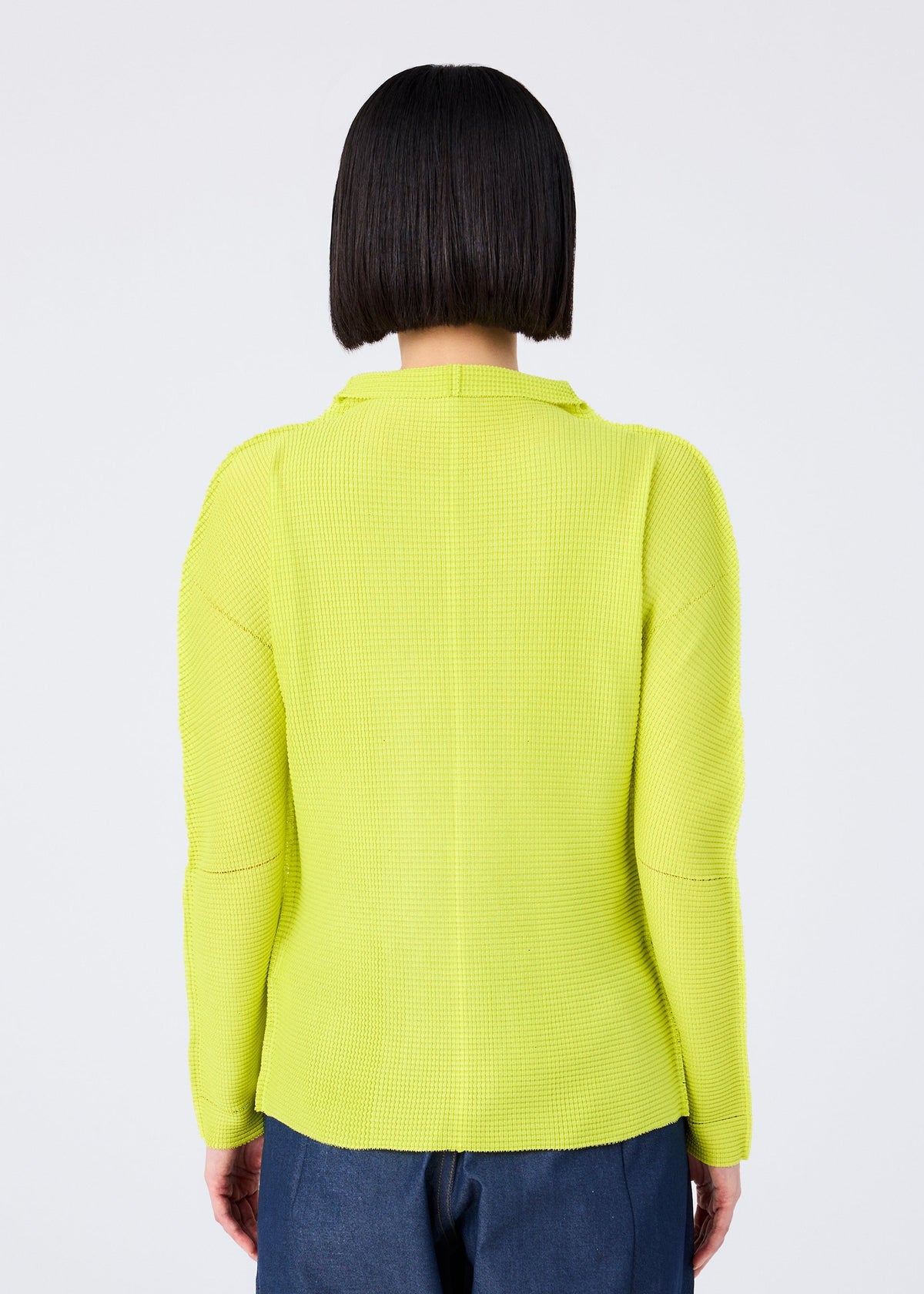 A person with a straight, chin-length bob is shown from behind wearing me ISSEY MIYAKE’s KNIT STRETCH PLEATS 1 top in bright yellow with long sleeves and dark blue pants, set against a plain light background. view 7 of 8