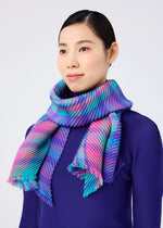 A woman with straight dark hair wears the CHECK PLEATS STOLE from me ISSEY MIYAKE—a vibrant, yarn-dyed piece with blue, purple, pink, and turquoise stripes—draped over a textured deep purple top against a light background.