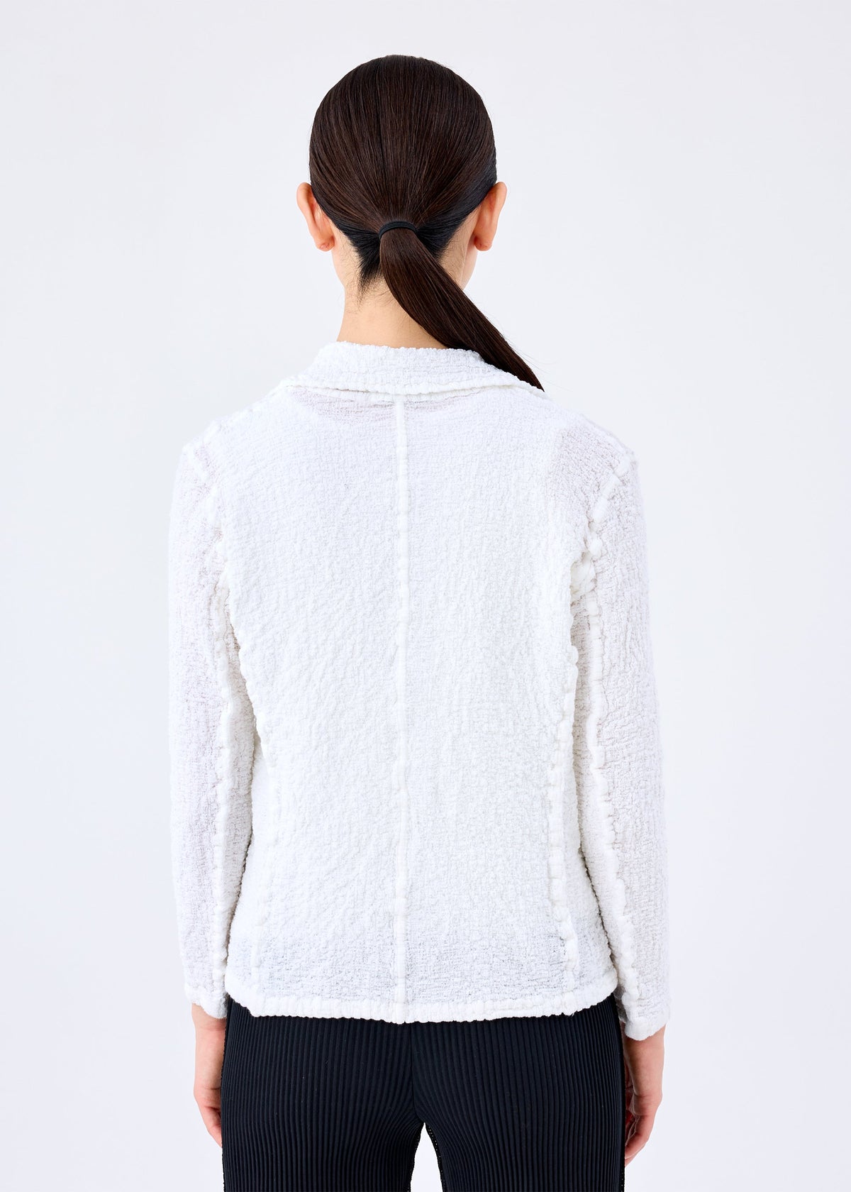 A person with straight dark hair in a low ponytail is shown from behind, wearing the white textured CAULIFLOWER JACKET by me ISSEY MIYAKE and black pants against a plain light background. view 5 of 6